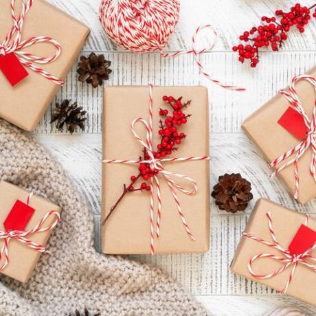 handgemachte weihnachtsgeschenke flach mit kiefernzapfen, in kraftpapier gewickelte geschenke und verziert mit gestreifter bäckerschnur und stechpalmenbeeren auf dem holzhintergrund