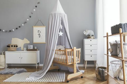 Interior elegant pentru camera nou-născutului scandinav cu afiș machetat, mobilier alb, jucării naturale, baldachin gri suspendat cu stele și urși de pluș. Interior minimalist și confortabil al camerei pentru copii.