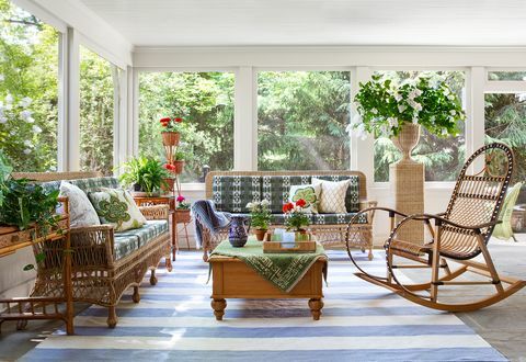 מוקרן במרפסת, שטיח מפוספס בכחול ולבן, כסאות נצרים וספה עם כריות ירוקות ולבנות, צמחים פנימיים