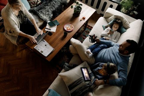 ภาพมุมสูงของครอบครัวโดยใช้เทคโนโลยีต่างๆ ในห้องนั่งเล่นที่บ้าน