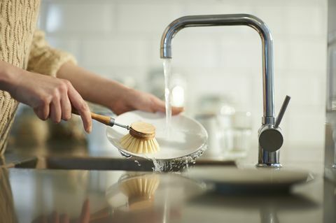 o femeie folosește o perie fără plastic pentru a curăța vasele dintr-o chiuvetă de bucătărie, de aproape
