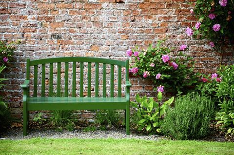 Zelená záhradná lavička v svetlej záhrade proti tehlovej stene
