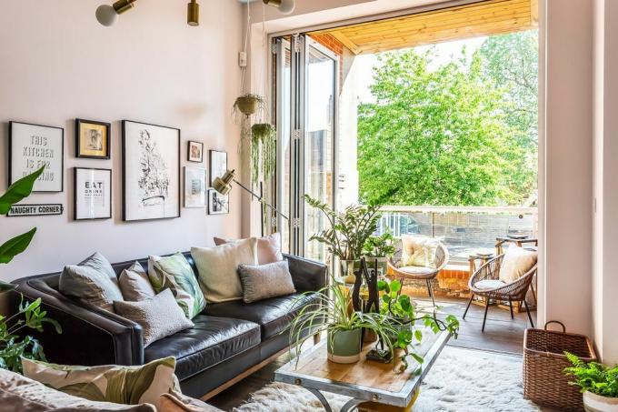 un living contemporan cu canapea și perete de galerie, cu uși pliante care se deschid spre o terasă cu copaci în fundal