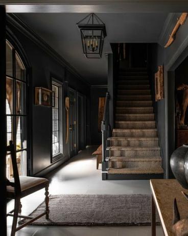 vchod, schody, schodiště pokryté kobercem, bílé dlaždice, černě natřené stěny, lišta s černou korunou