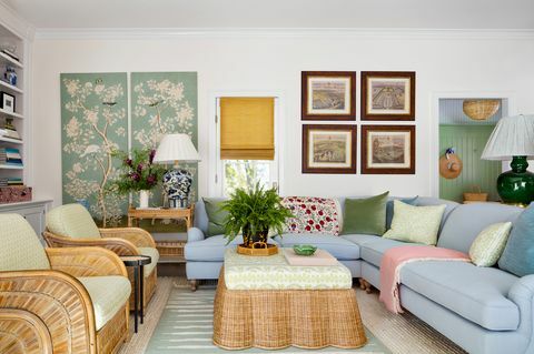 angol szoba, kék kanapé heverő, fonott dohányzóasztal zöld -fehér kanapé párnával és zöld -fehér díszpárnákkal, rózsaszín dobószőnyeg, nagy zöld lámpa