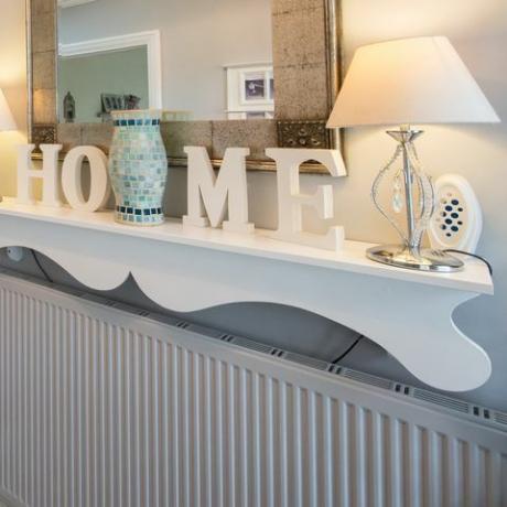Ein allgemeiner Blick auf einen Flur mit schwarz-weiß kariertem Fliesenboden, einem verzierten Regal aus blanker Holztreppe mit den Buchstaben, die das Wort Zuhause buchstabieren