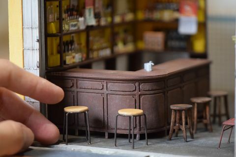 närbild av en miniatyrreplik av en bar, med barstolar och en mänsklig hand för skala