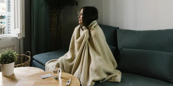 zieke vrouw die wegkijkt terwijl ze thuis in een deken is gewikkeld