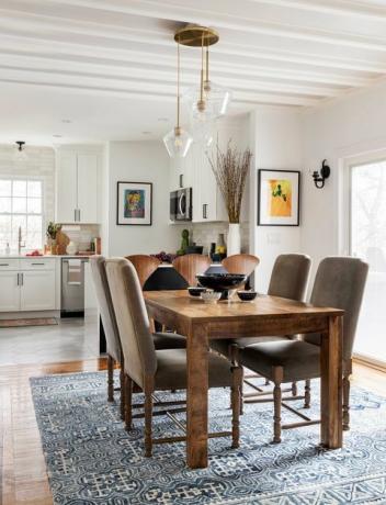 dřevěný jídelní stůl, hnědé kožené jídelní židle, modrý a bílý koberec, nástěnné umění, kolekce misek