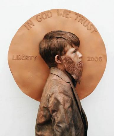 menino com barba falsa e terno pintado de marrom em pé de perfil na frente de uma grande moeda falsa