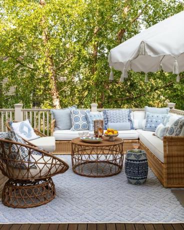 kanapa ogrodowa, białe poduszki na siedziska z gamą niebieskich i białych poduszek dekoracyjnych, niebieski dywanik ogrodowy, niebiesko-biały stolik