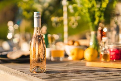 neatvērta pudele auksta rozā vīna uz vasaras vakariņu galda Zviedrijā, koncentrējoties uz pilošu svaigu pudeli priekšplānā