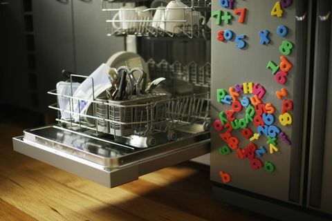 Машина за прање судова са отвореном фиоком поред фрижидера прекривена дечијим магнетима за фрижидер