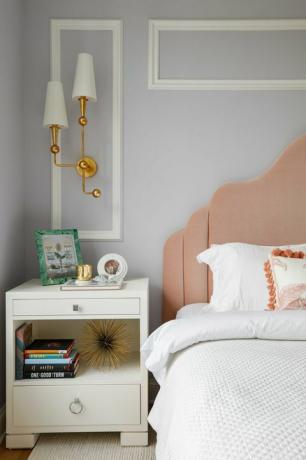 ベッドルーム、白いリノンのベッド、白いベッドサイドテーブル、本、ピンクのヘッドボード、白と金の燭台、ライトグレーブルーの塗られた壁に白い王冠の成形