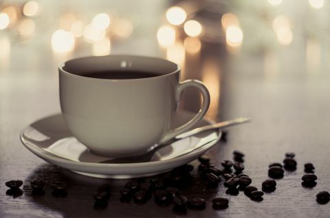 Чашка и блюдце с кофе стояли на столе, усыпанном кофейными зернами.