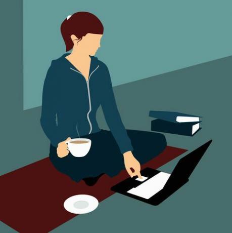 Жена седи на поду са шољом чаја и користи лаптоп