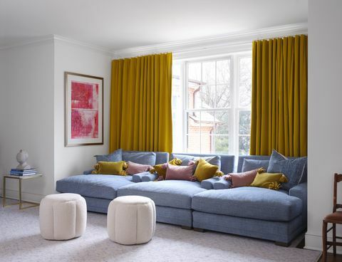 mėlyna sofa, geltonos užuolaidos, rožinės ir geltonos pagalvėlės