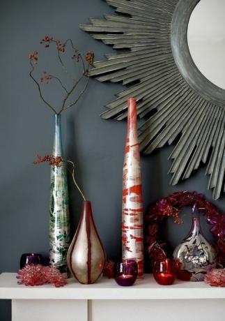 црвене и плаве стаклене вазе са аранжманом од гранчица, свећњаци, оквир камина, огледало од сунчевог зрачења, божићни венац, свечани, насупрот сивог зида