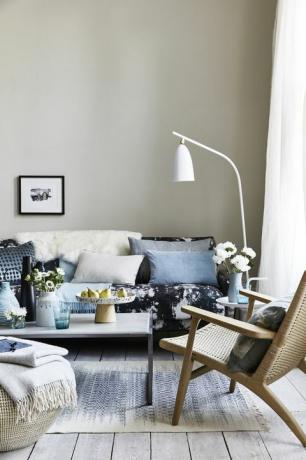 гостиная с подушками на диване с синим рисунком, белый торшер, наклоненный над полом, пятна и блики для создания импрессионистского образа, современного и расслабленного.