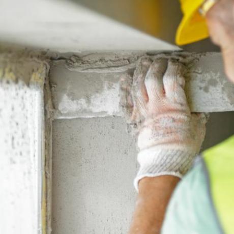 Οπίσθια όψη εργατών οικοδομών που ισοπεδώνουν τον τοίχο παραθύρου με τσιμέντο και αλφάδι στο σπίτι