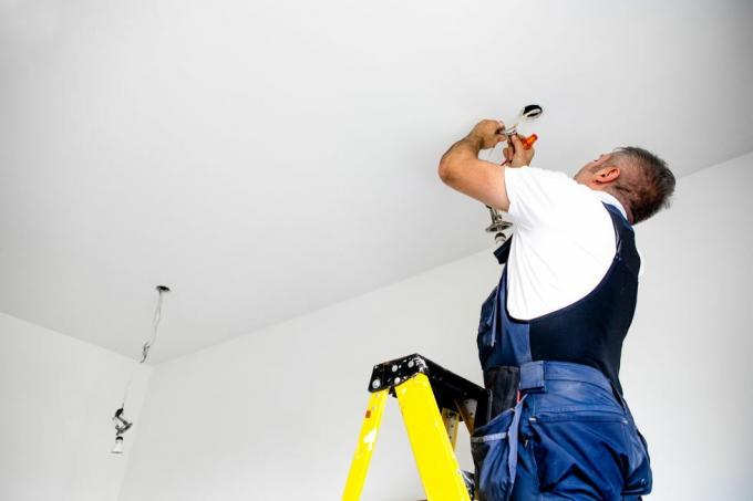 ремонтник мужчина-электрик чинит свет, устанавливая светодиодный светильник в потолочный светильник
