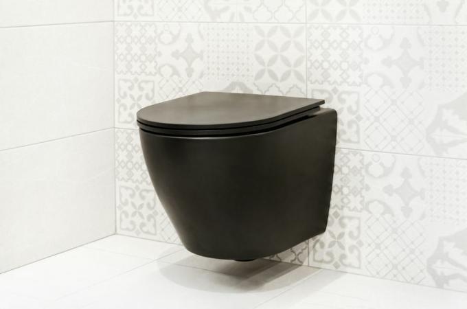 흰 벽에 걸린 검은색 변기 타일 욕실 내부에 있는 현대적인 벽걸이형 변기