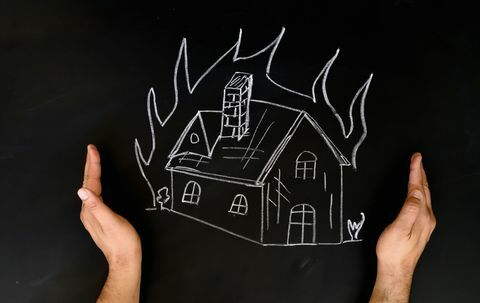 Hausversicherungskonzept Mann schützt Haus mit den Händen vor Feuer