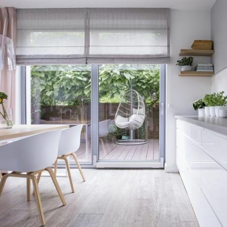 Závěsná židle na dřevěné terase moderního domu s bílým kuchyňským interiérem