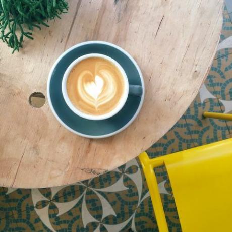 Kopje koffie met hartschuim in groenblauwe mok op houten tafel