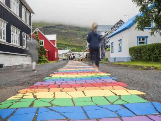 Island, Seydisfjördur, Menschen, die mitten in einer abgelegenen Stadt auf einer regenbogenfarbenen Asphaltstraße spazieren