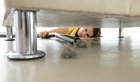 Kvinna som når under en soffa för att komma åt lite damm