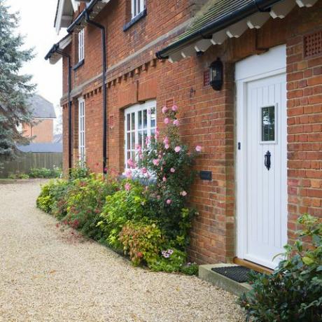 Casa de campo inglesa y jardín en otoño con un camino de grava, la casa es de época victoriana, con bordes de flores llenos de arbustos y plantas perennes