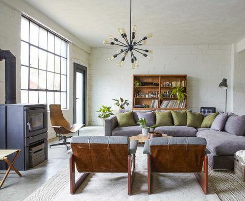 pelēks dīvāns, betona grīdas, zaļi spilveni, malkas krāsns