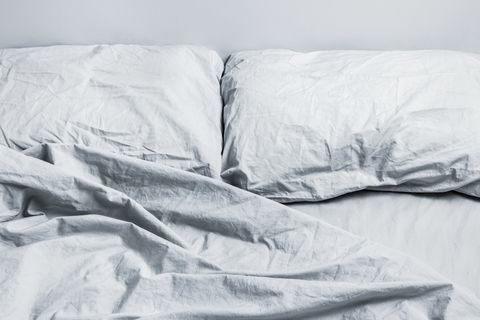 netīra pelēka gultas veļas gulta ar diviem spilveniem dienasgaismā