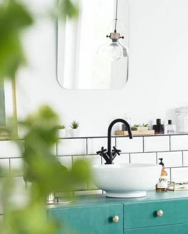 Nahaufnahme von verschwommenen Blättern mit Waschbecken, grünem Schrank und Spiegel im Hintergrund im echten Foto des Badezimmerinnenraums