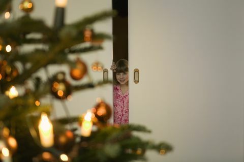 ילדה בפיג'מה מציצה מבעד לדלת לעץ חג המולד