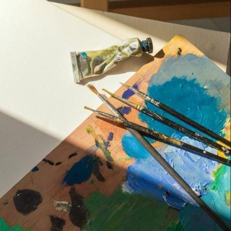 materiály na maľovanie prázdneho plátna, paleta plná farebných farieb, štetce a tuby na olejové farby pripravené na maľovanie doma