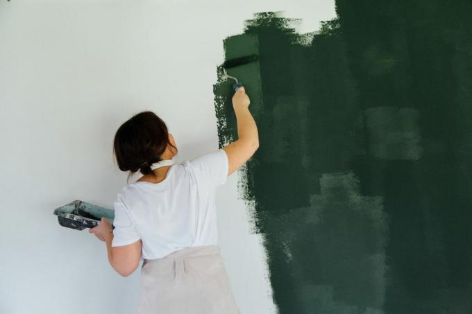 白い壁を緑色で塗るヘッドフォンの女性