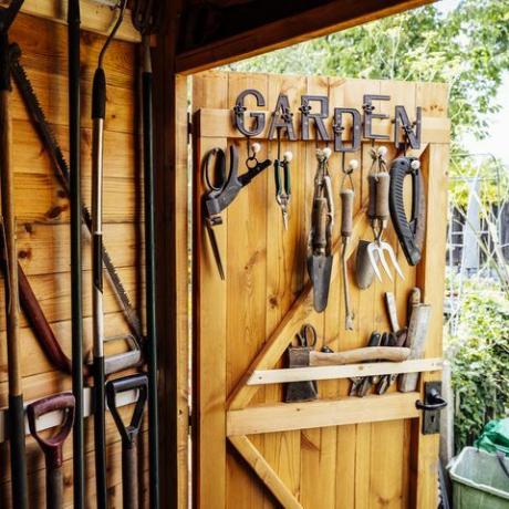 binnenaanzicht met open deur van georganiseerde schuur gevuld met hark, schoppen, trimmer, zaag en ander handgereedschap dat nodig is voor het onderhoud van een goed onderhouden tuin