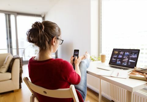 Frau sitzt zu Hause am Schreibtisch mit Smartphone