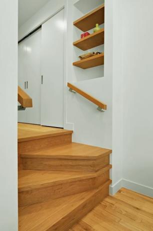 Tangga saku: tangga empat langkah modern khusus mengarah ke lorong, membentuk pendaratan mini dengan rak buku di tengah jalan.