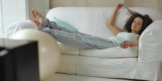 жена, лежаща на дивана, използваща дистанционното управление на телевизора